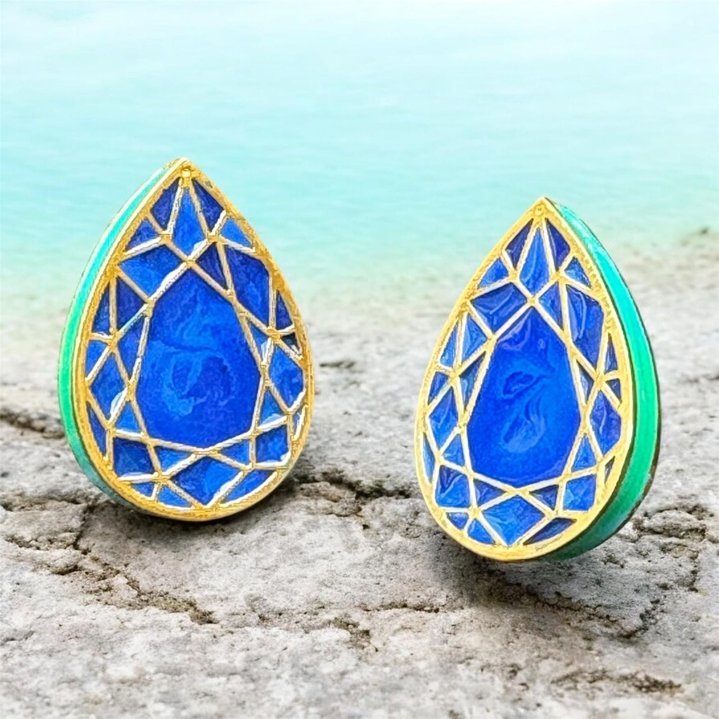 Teardrop-shaped earrings with blue and gold design on a textured surface.