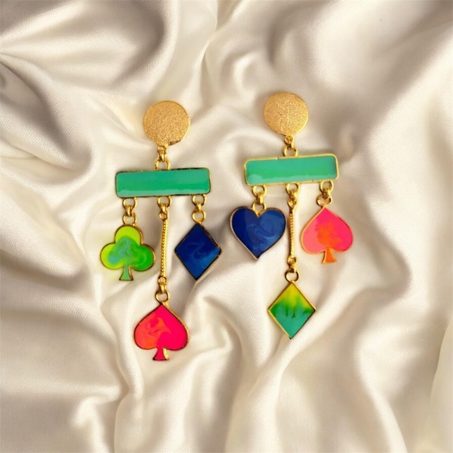 Colorful card suit earrings on a satin background