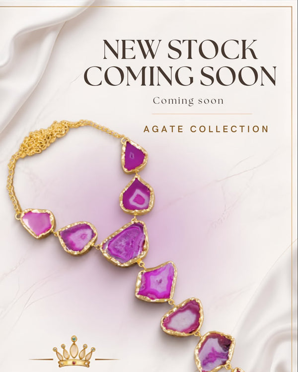Promotional banner for the 'Agate Collection' by Banca Bling, featuring a gold necklace with irregular purple agate gemstones. The image includes a 'NEW STOCK COMING SOON' text overlay and a 'BANCA BLING' brand logo at the bottom, set against a background of draped white satin fabric.