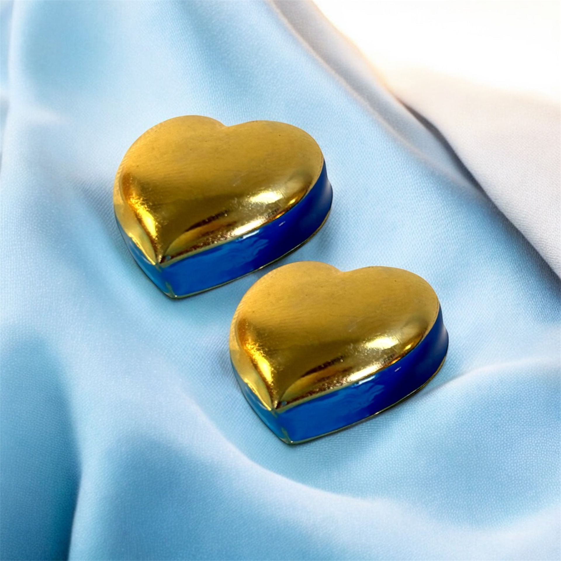 Heart-shaped gold and blue earrings on a light blue fabric background