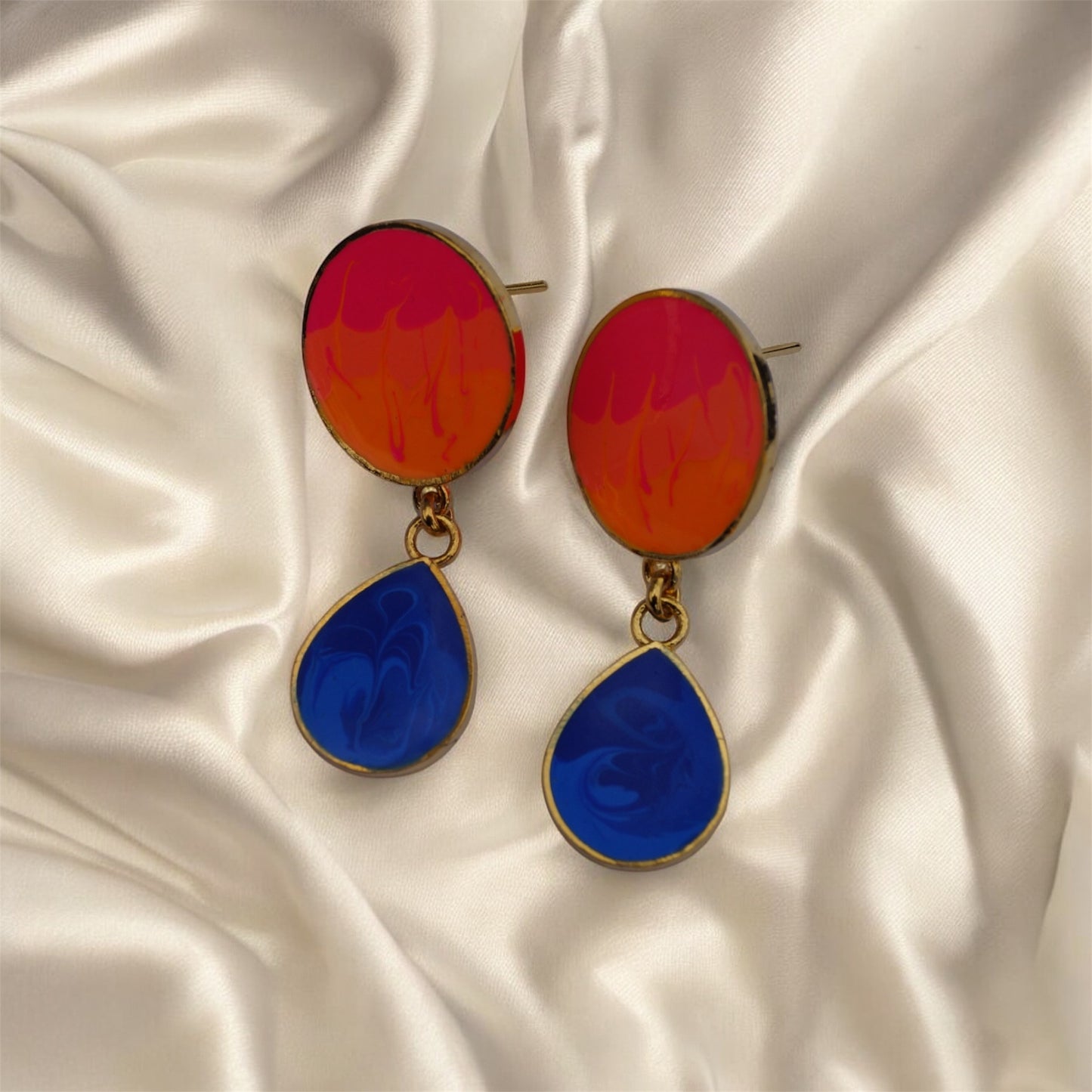 Colorful earrings with red and blue droplets on a satin background