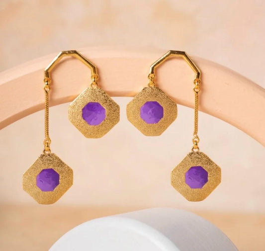 Gold earrings with purple stones on a beige background