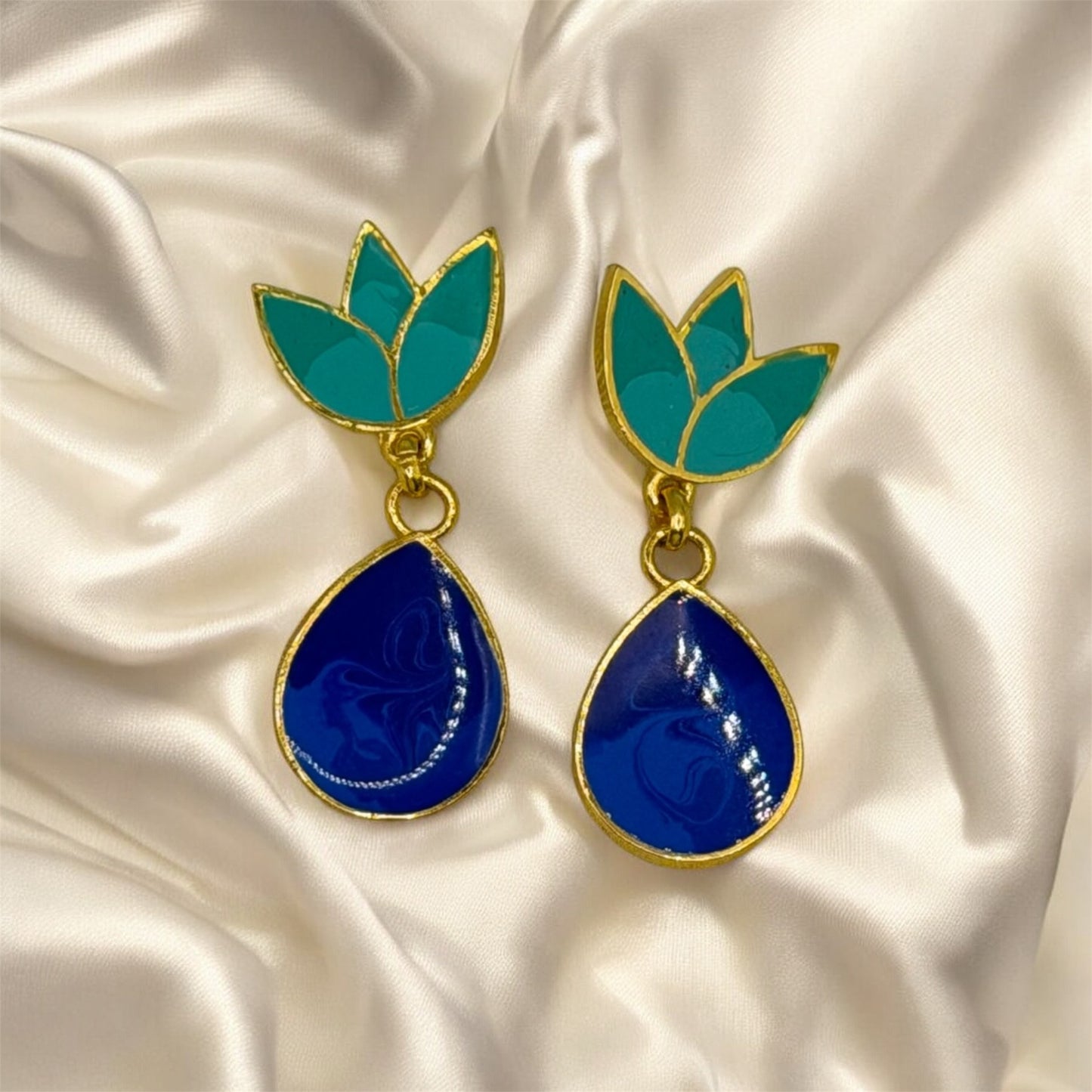 Pair of earrings with blue teardrop and green leaf-like top on a satin background