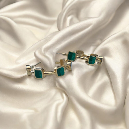 Gold and green square stud earrings on a satin surface