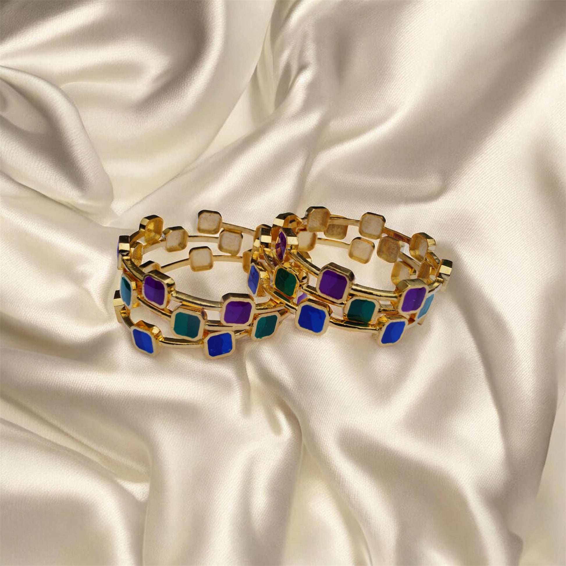 Gold bracelets with colorful square stones on a satin background