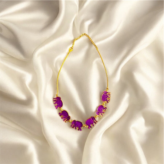 Gold necklace with purple elephant pendants on a satin background